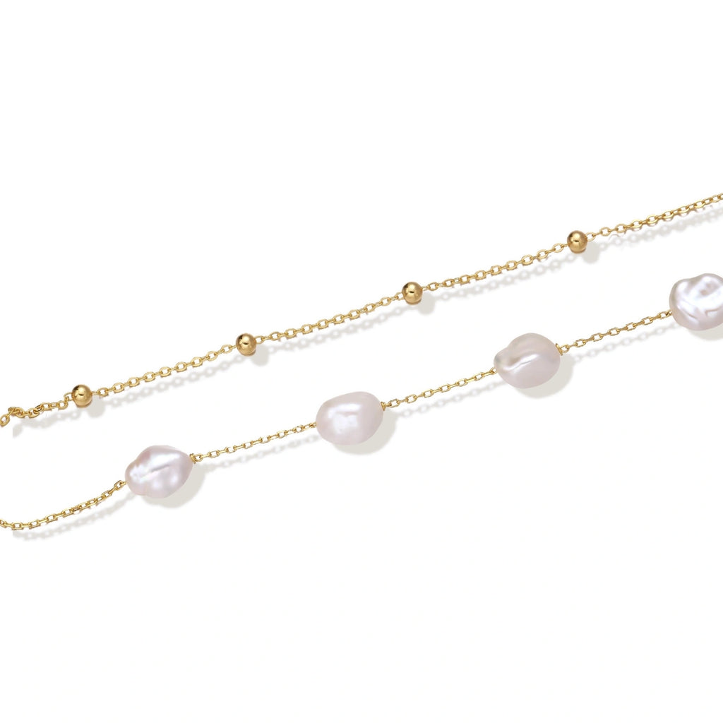 Double-strand gold bracelet with irregular baroque pearls and smooth freshwater pearls on cream background.