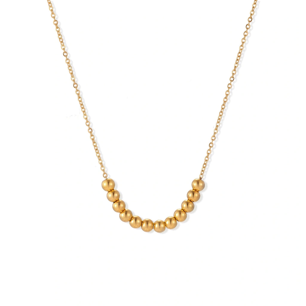 Delicate gold-plated necklace with graduated spherical beads forming gentle smile curve on beige background