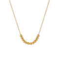 Delicate gold-plated necklace with graduated spherical beads forming gentle smile curve on beige background