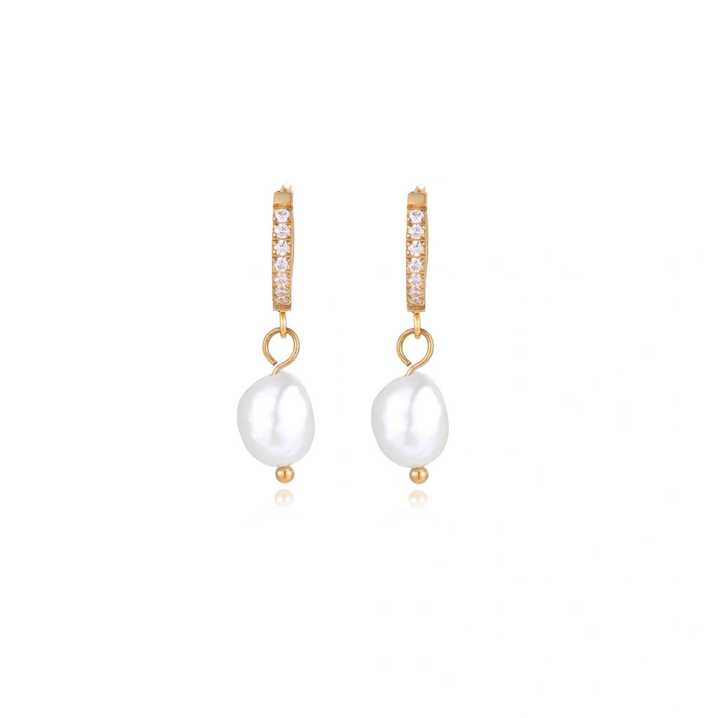 Gold huggie hoop earrings with pavé crystals and white freshwater pearl drops on cream background