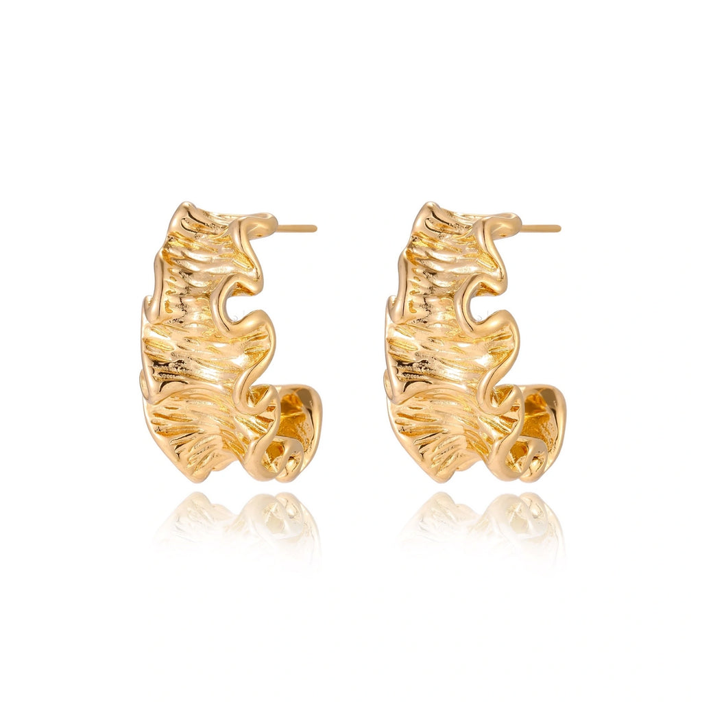 Pair of gold huggie hoops with sculpted wave texture and dimensional ripples on neutral background.