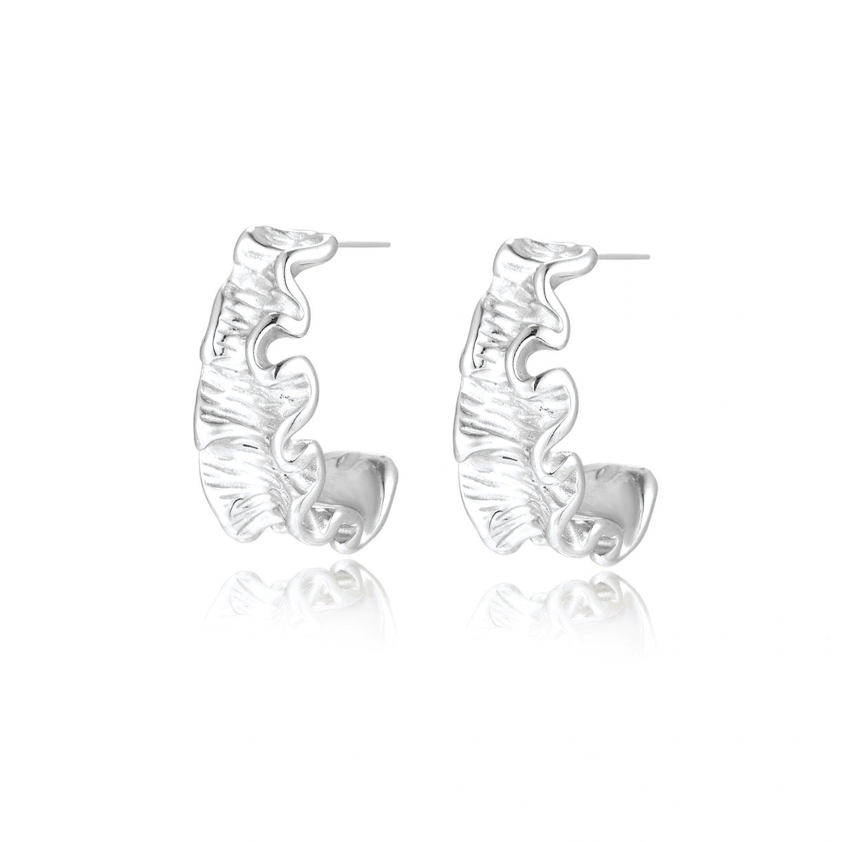 Textured white gold-plated hoop earrings with flowing wave pattern against cream background, showing dimensional rippled surface.