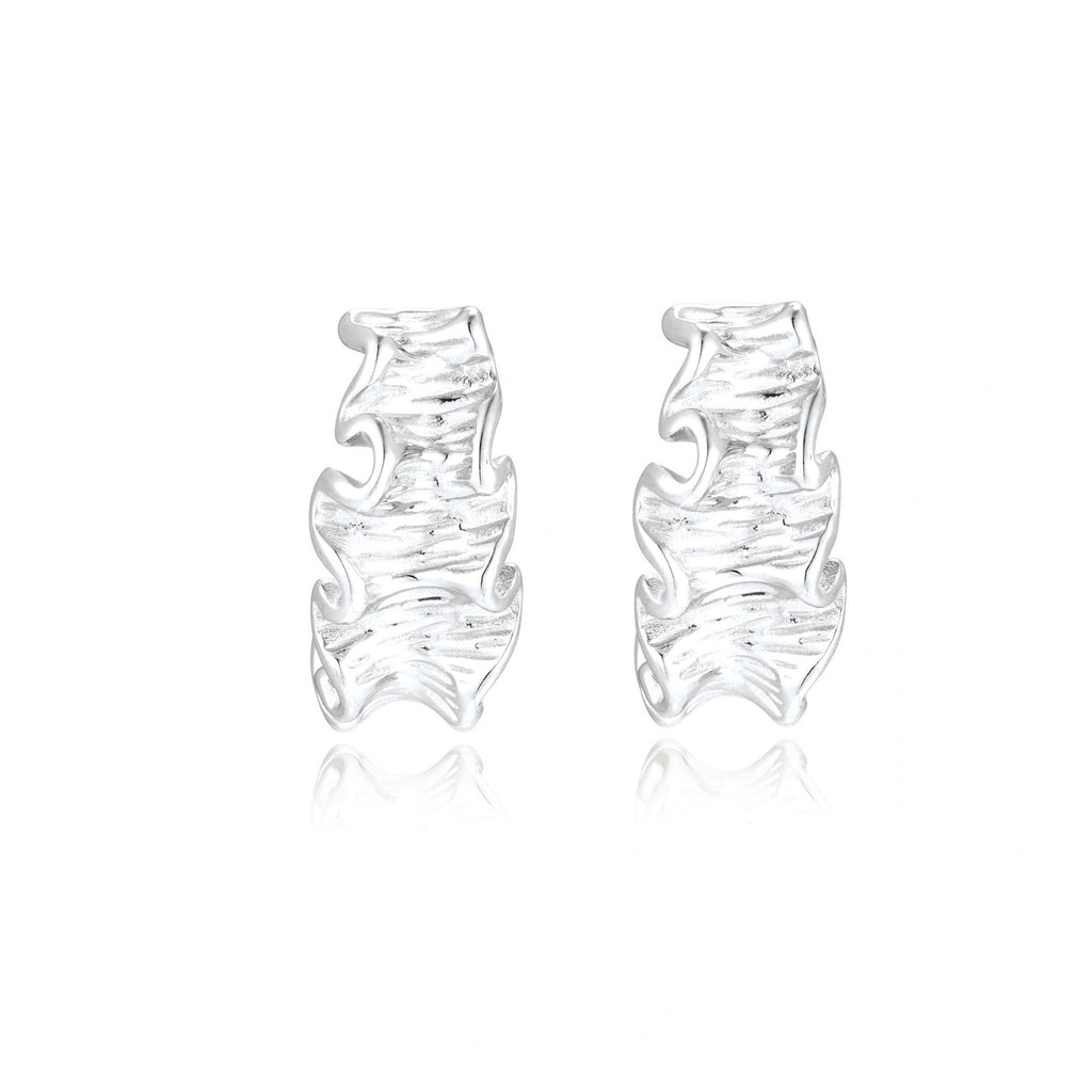 Textured white gold-plated hoop earrings with flowing wave pattern against cream background, showing dimensional rippled surface.
