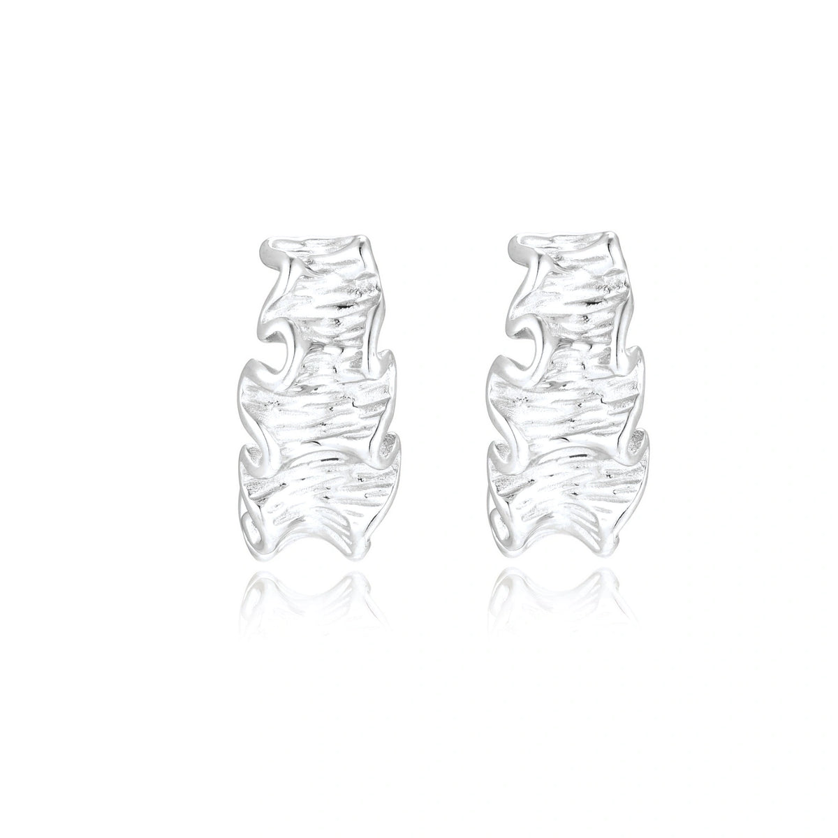 Textured white gold-plated hoop earrings with flowing wave pattern against cream background, showing dimensional rippled surface.