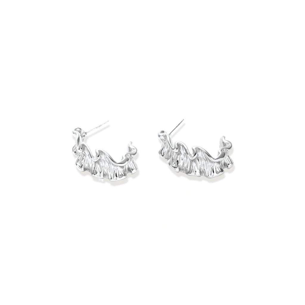 Textured white gold-plated hoop earrings with flowing wave pattern against cream background, showing dimensional rippled surface.