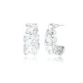 Textured white gold-plated hoop earrings with flowing wave pattern against cream background, showing dimensional rippled surface.