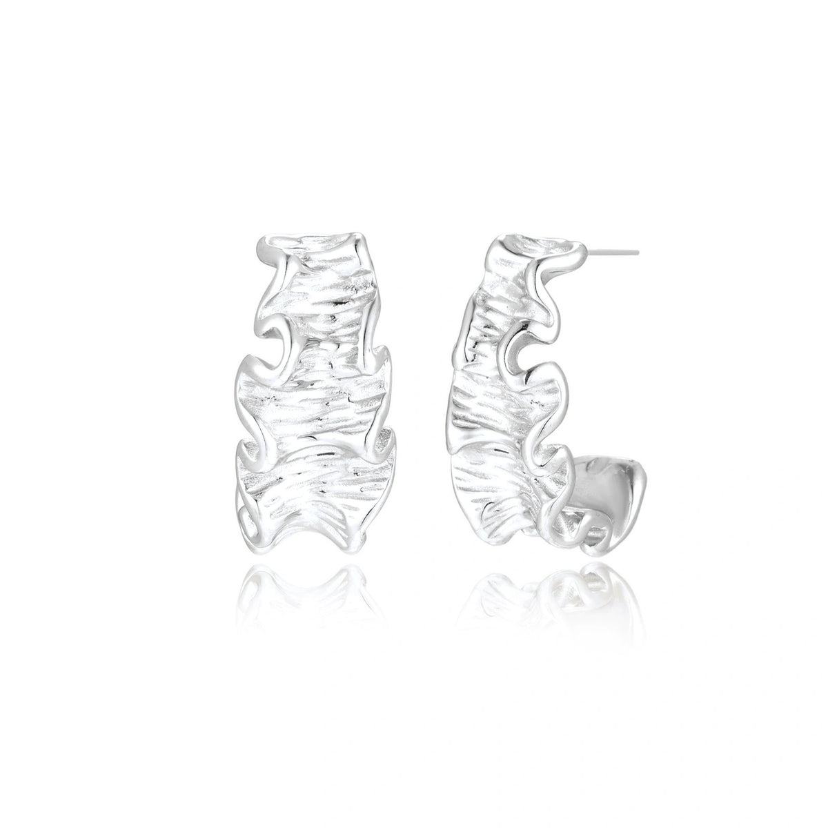 Textured white gold-plated hoop earrings with flowing wave pattern against cream background, showing dimensional rippled surface.
