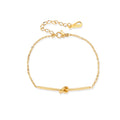 Delicate gold chain bracelet with minimalist bar and centered knot detail on cream background