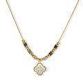 Gold-toned beaded necklace with grey stones and quatrefoil abalone shell pendant on cream background.